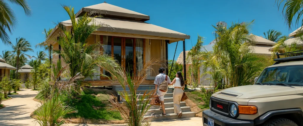 A couple holding hands as they walk up the steps to a luxury tented bungalow at a Costa Rica resort with an SUV parked nearby.