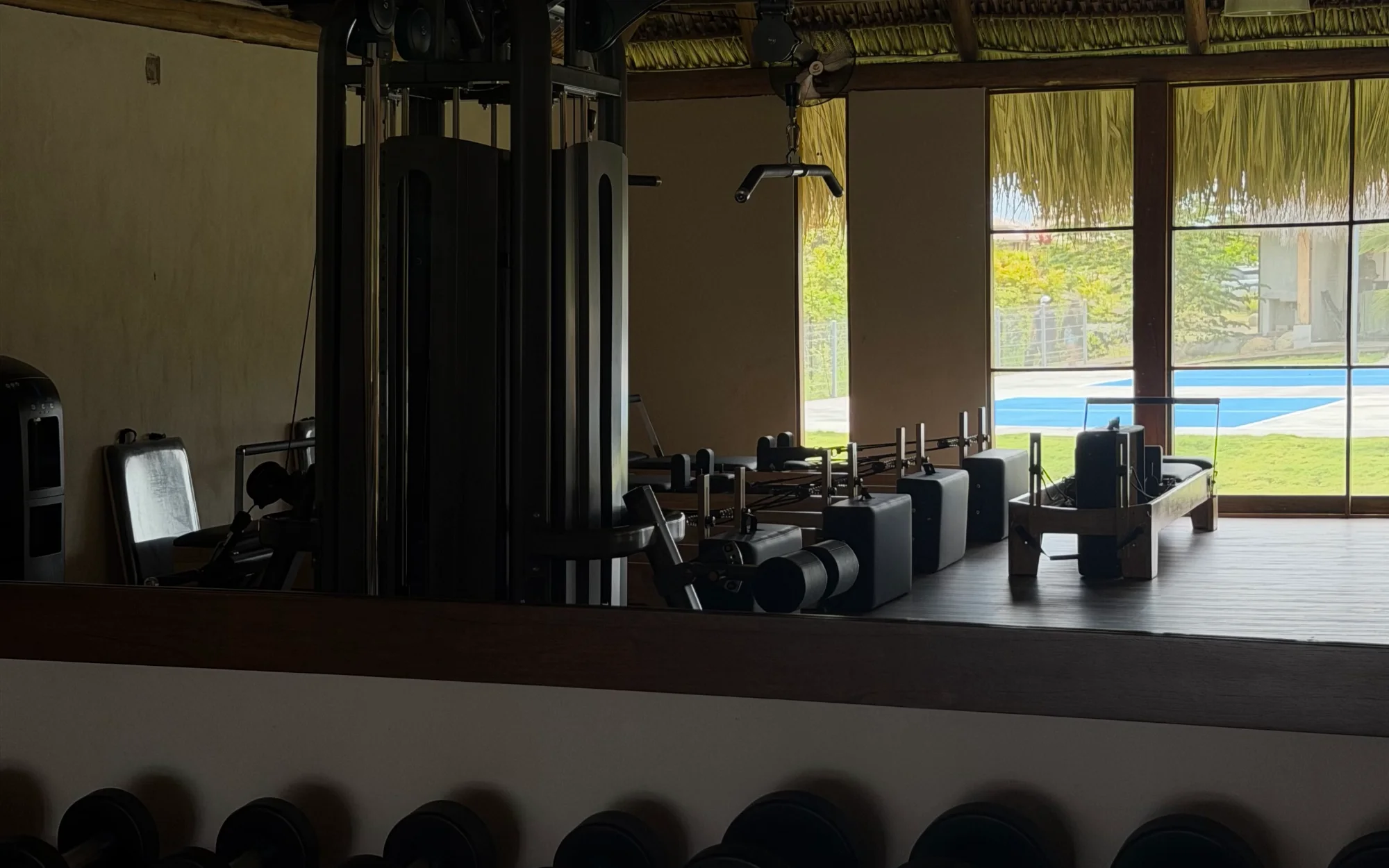 Rack de mancuernas y máquina de poleas en el gimnasio Madresal Active, con reformers de Pilates y la piscina tras los ventanales
